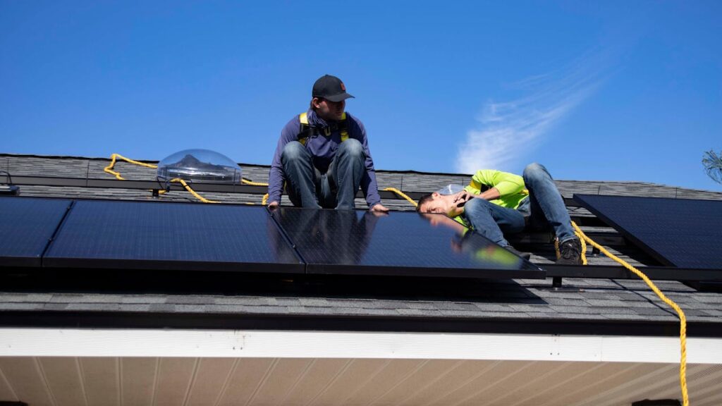 Two workers installing solar panels on the roof