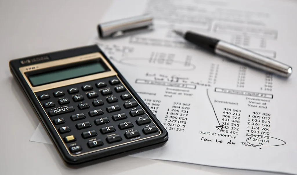 A calculator, a piece of paper and a pen on a white surface.