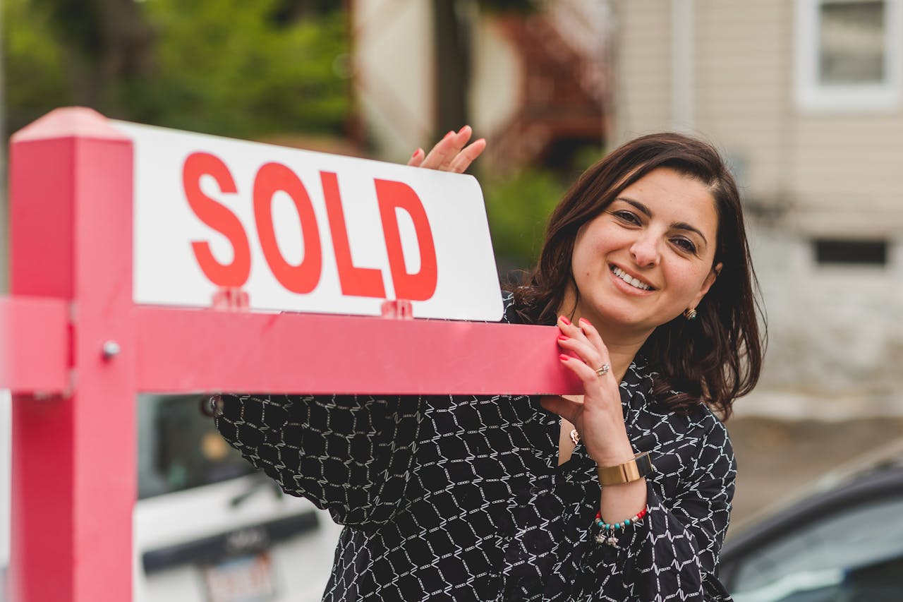 A real estate agent smiling next to a sold signage.